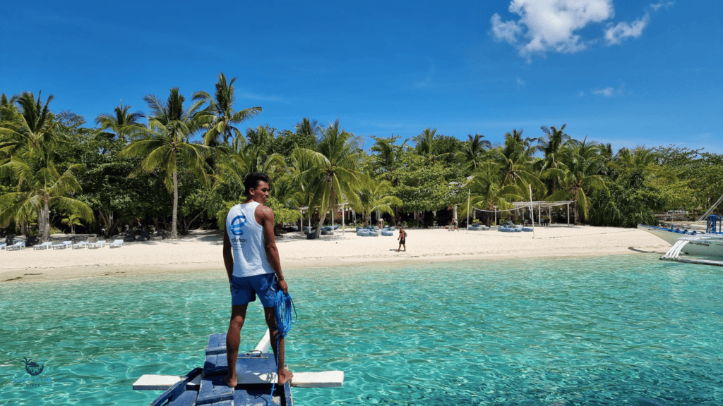 man on boat approaching white sandy beach with clear turquoise waters and palm trees